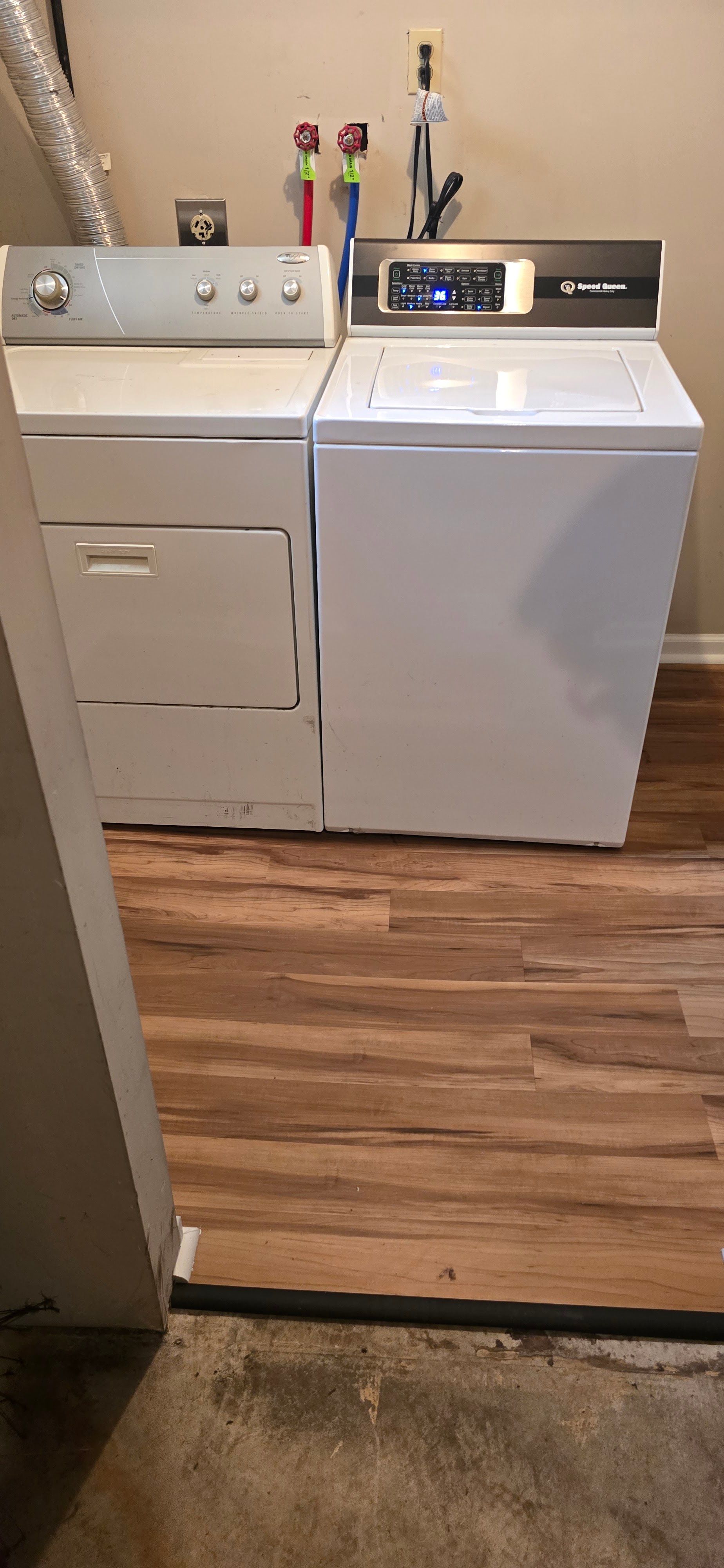 Laundry room with a white washer and dryer on a wood floor, with cleaning items on top.