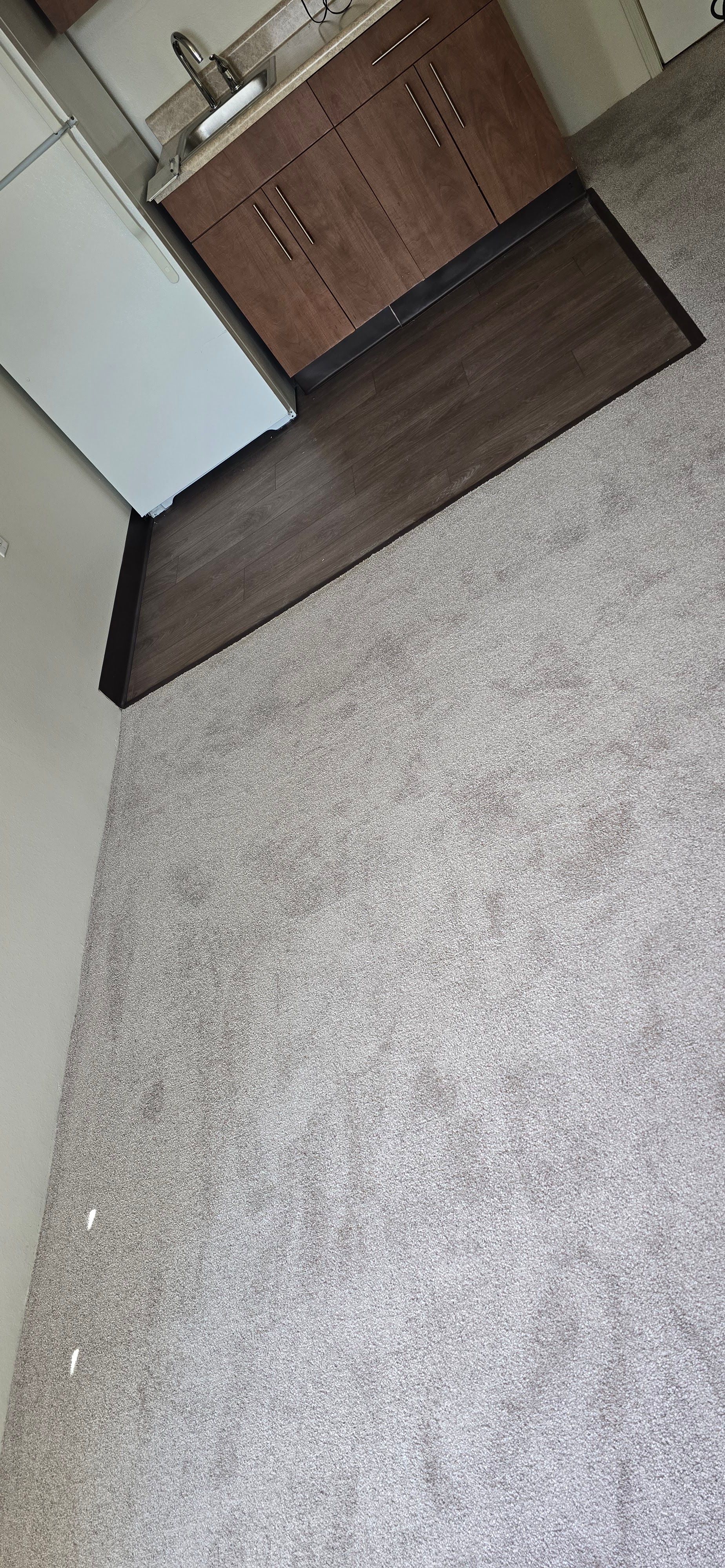 Carpeted hallway with a dark wood bench against a white wall and a wooden cabinet at the end.