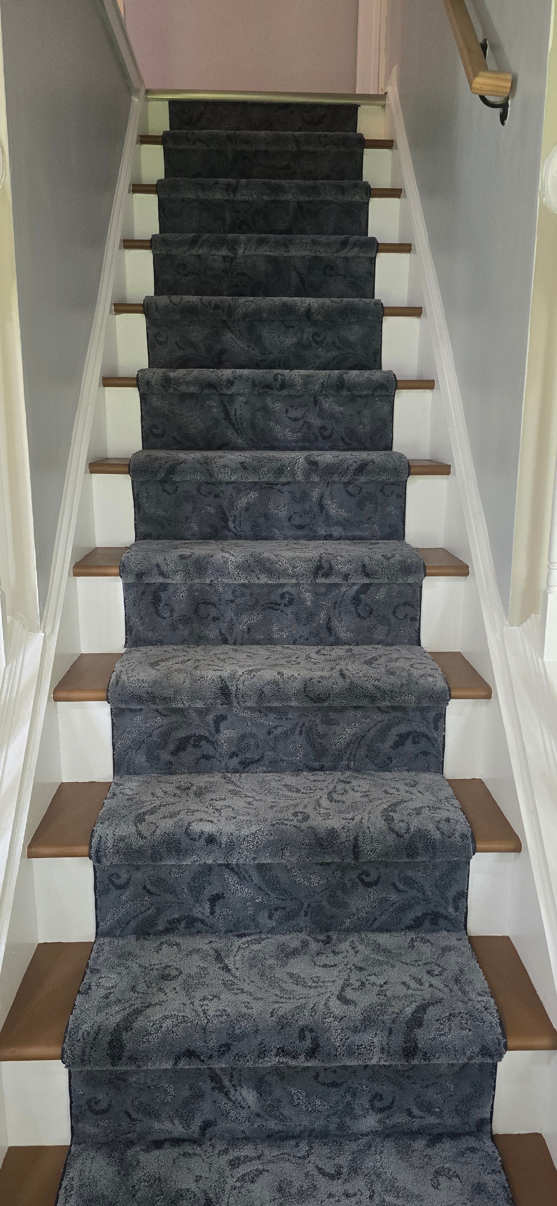 Carpeted staircase with dark runner leading up between white walls and wooden trim