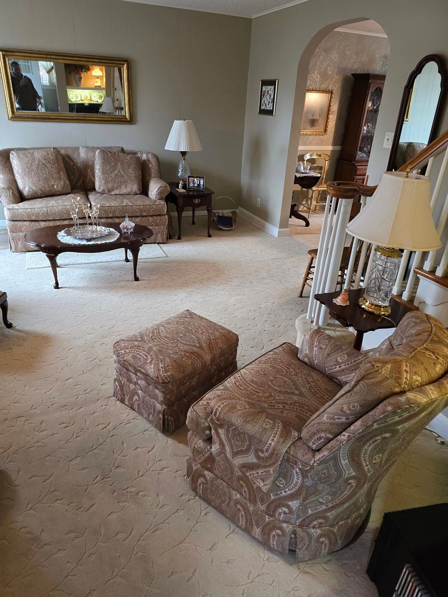 Living room with patterned sofas, matching ottoman, lamp, mirror, and beige carpet