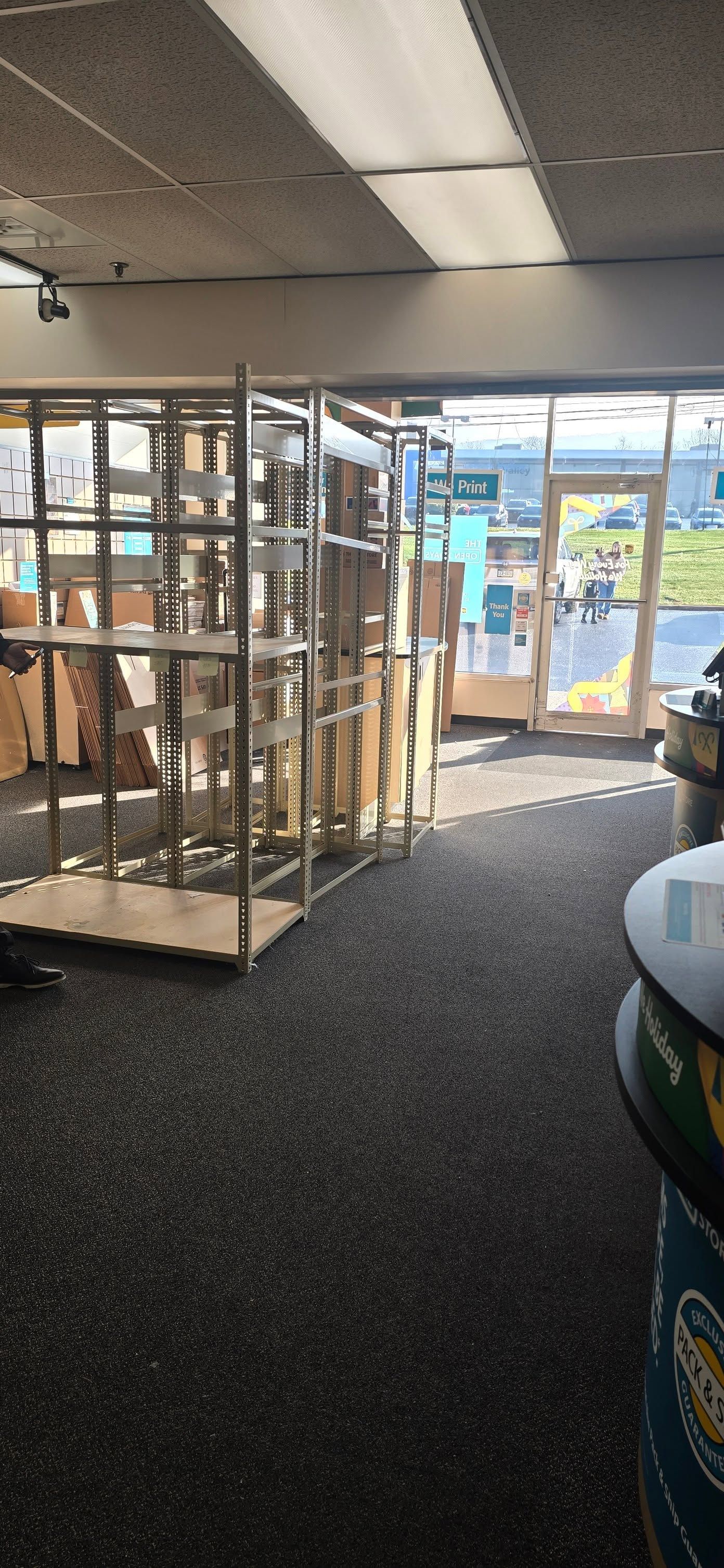 Empty storefront interior with shelves, dark carpet, and glass doors letting in daylight