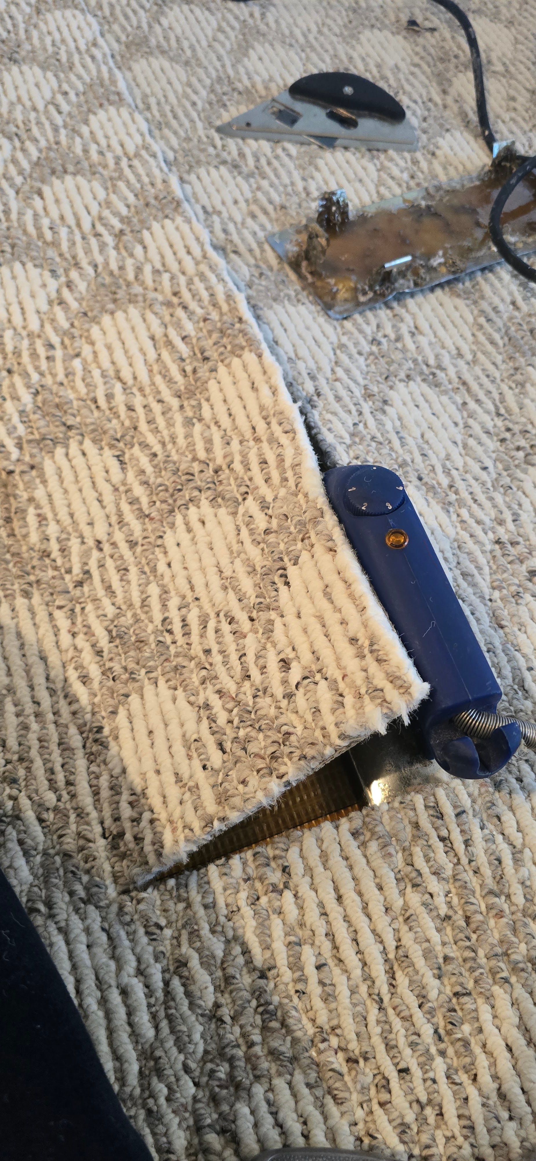 Blue handheld vacuum on a beige carpet beside a cord and power adapter.