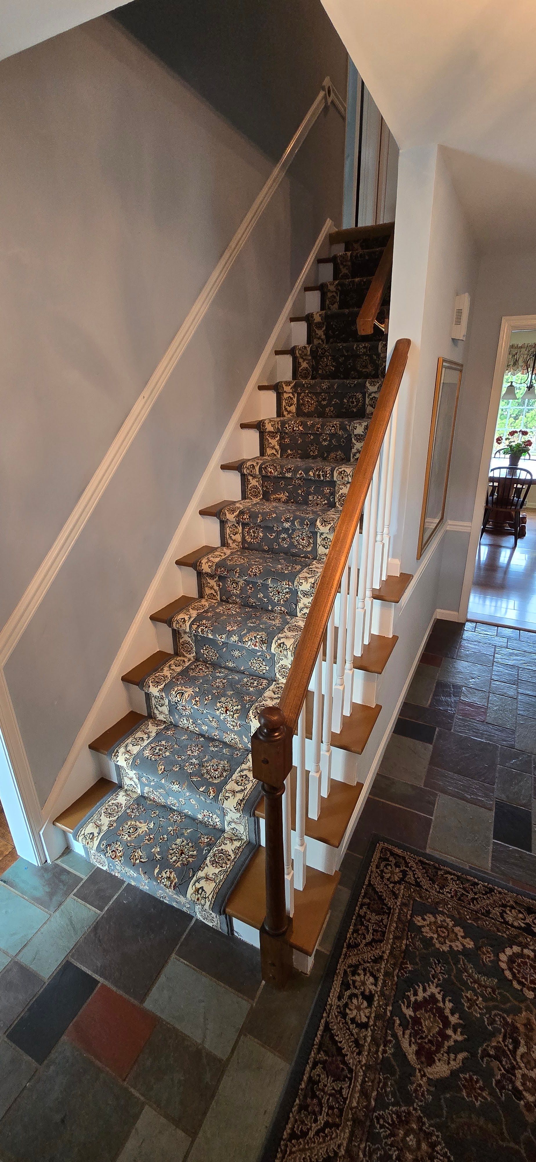 Indoor staircase with brown carpet runner, wooden banister, and tiled hallway.