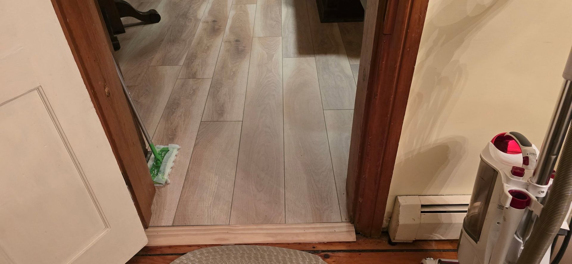 Hallway with a wood floor and doorway, showing a bathroom sink and toilet on the right and a radiator on the left