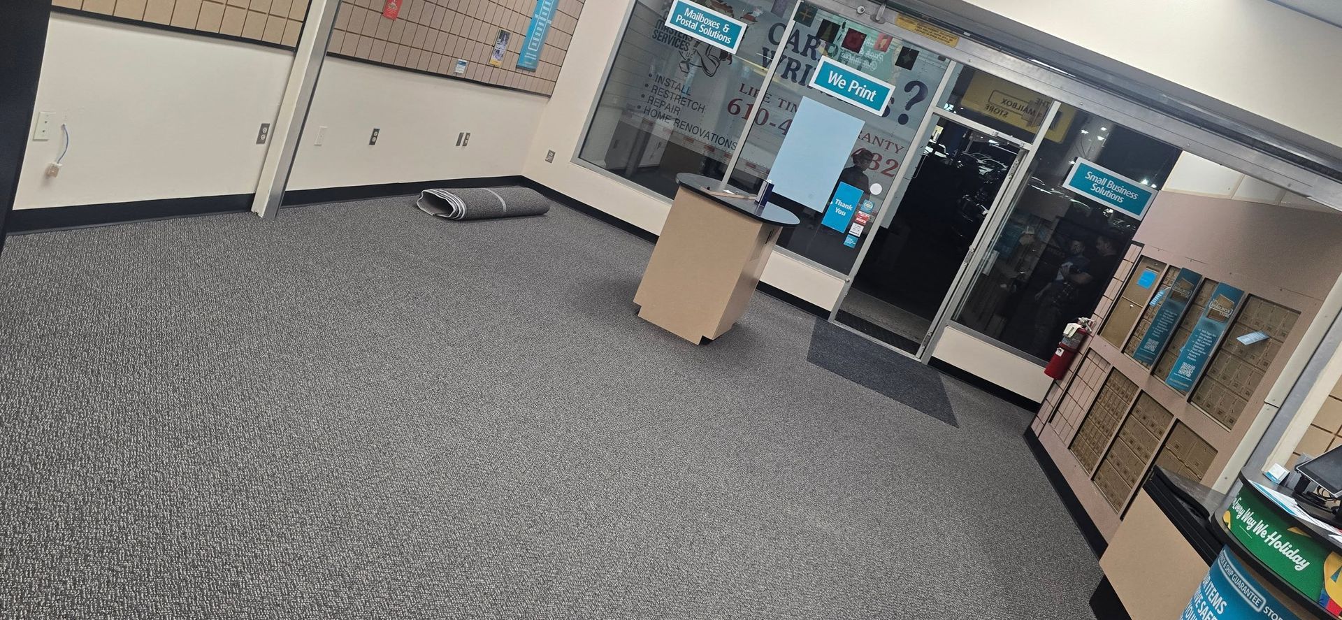 Empty office lobby with carpet, glass doors, cabinets, and a small wooden stand.