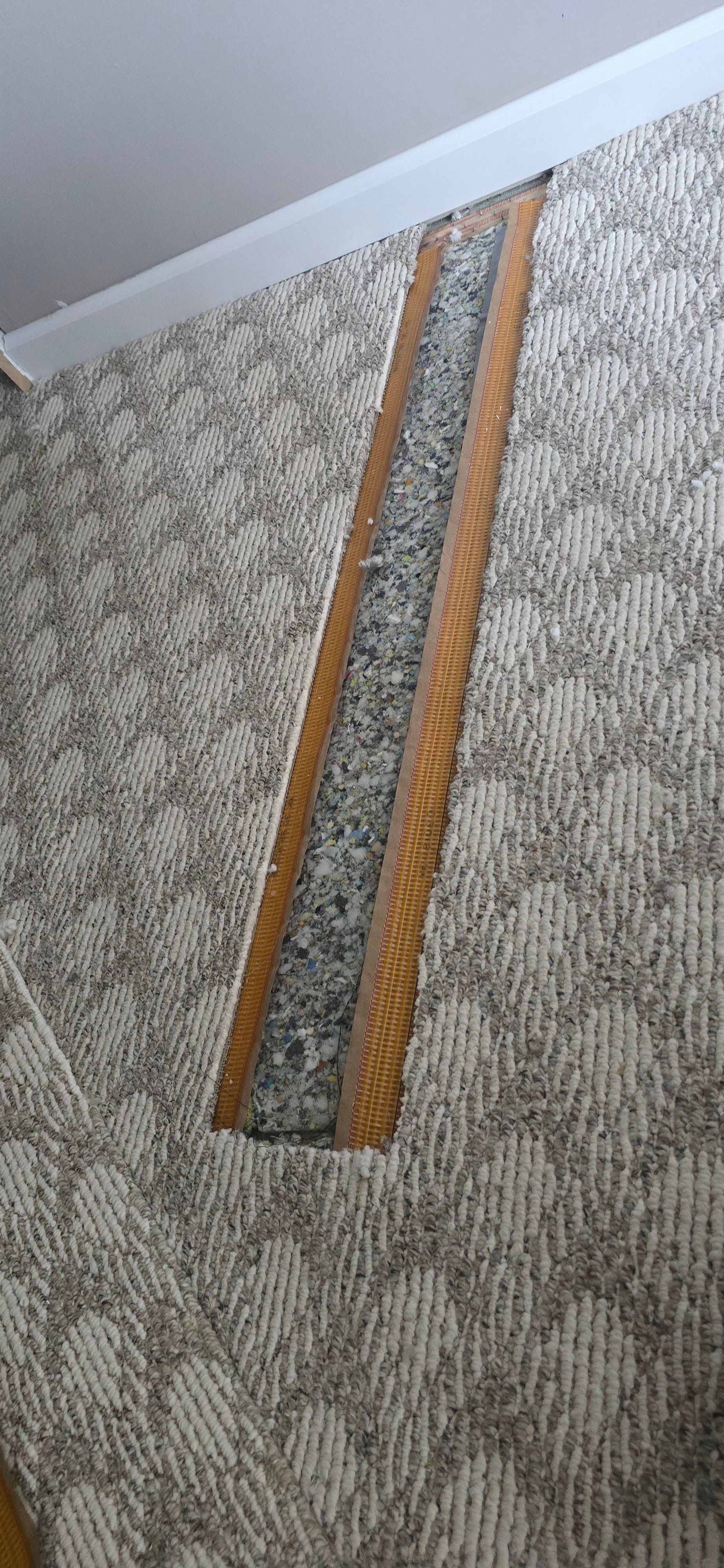 Two long orange-brown carpet strips on a gray patterned floor beside a white baseboard