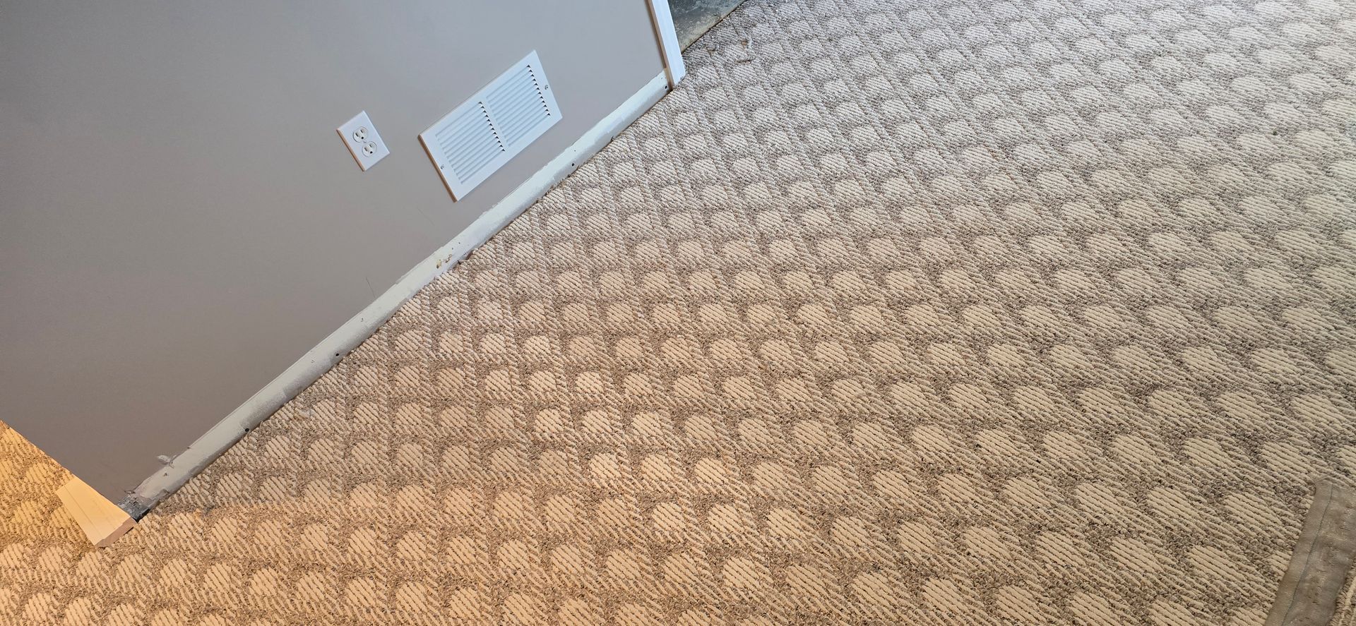 Carpeted hallway corner with beige walls, white vents, and a small window or door panel near the floor.