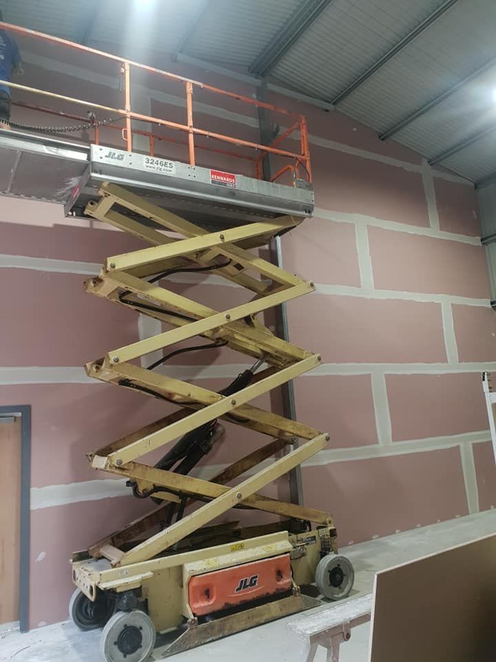 Scissor Lift Raised Indoors Beside a Pink Brick Wall and Metal Ceiling — Damien Thompson Plastering King Creek, NSW