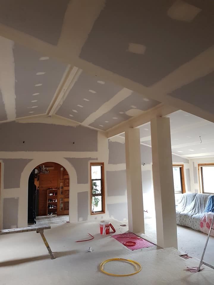 Unfinished room with drywall, exposed ceiling patches, columns, and construction materials on the floor.