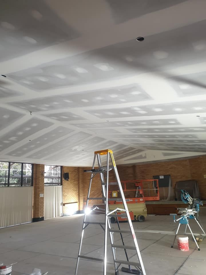 Empty room under construction with drywall ceiling, ladders, and tools on the floor