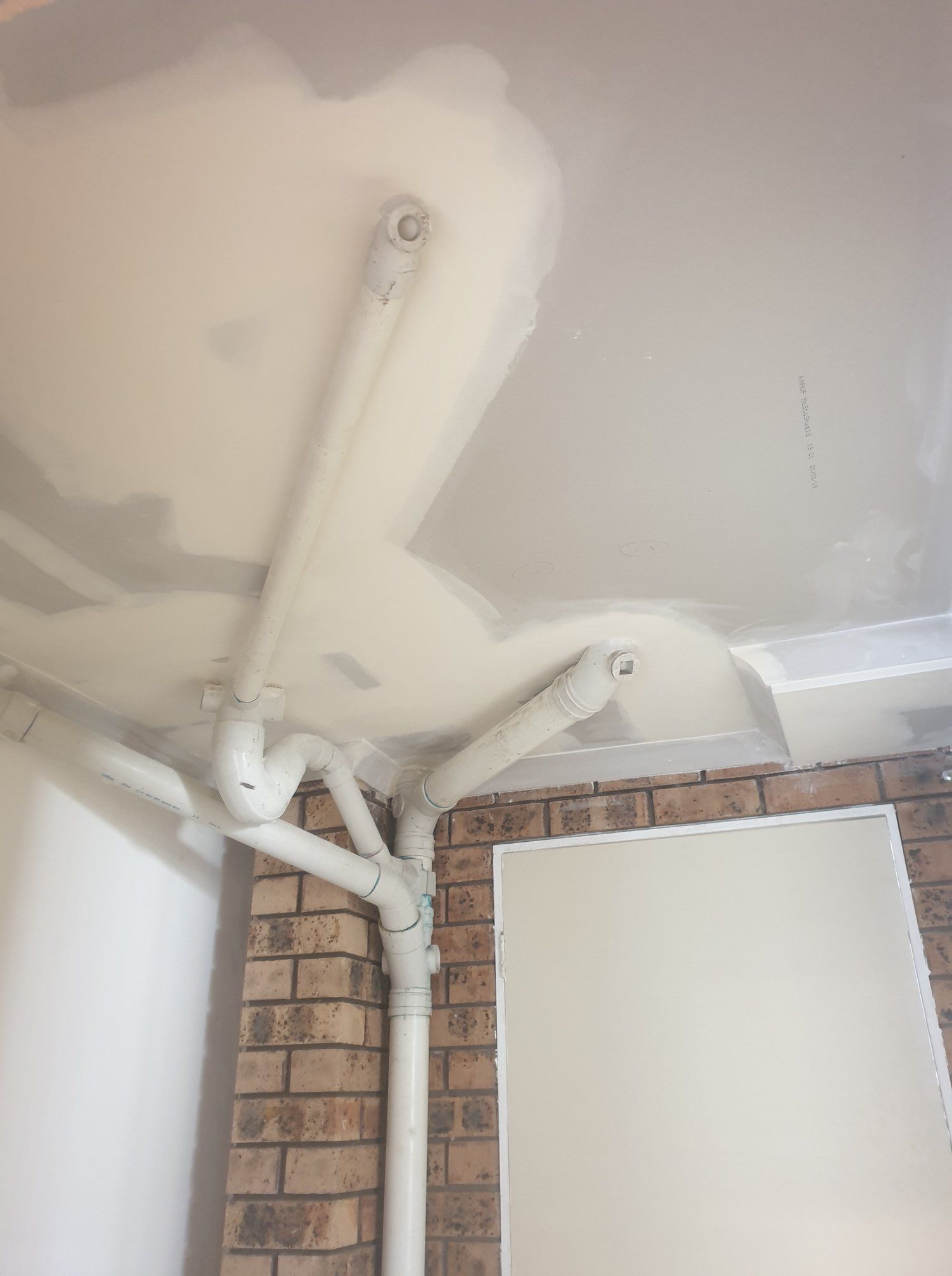 Ceiling Corner With White Pipes and Drywall Patches Above a Brick Wall — Damien Thompson Plastering King Creek, NSW