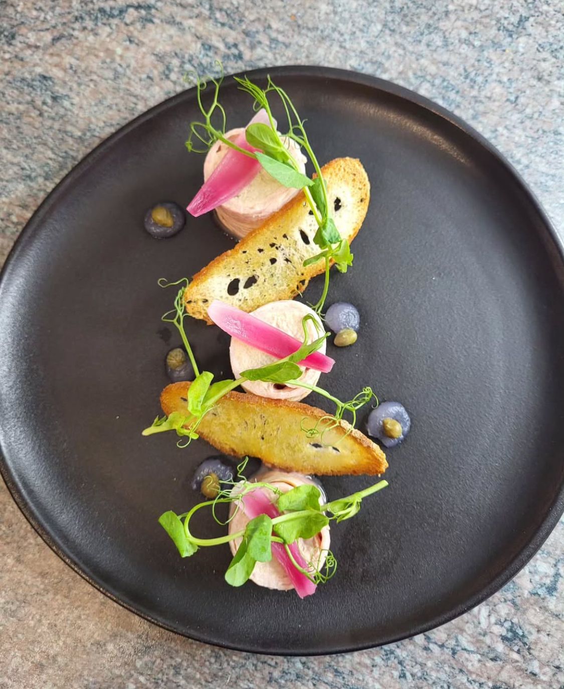 Une assiette noire surmontée de nourriture et de fleurs sur une table.