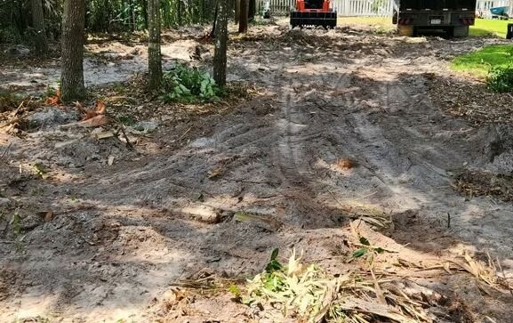 Dirt path through trees, showing tire tracks. Heavy machinery in the background.