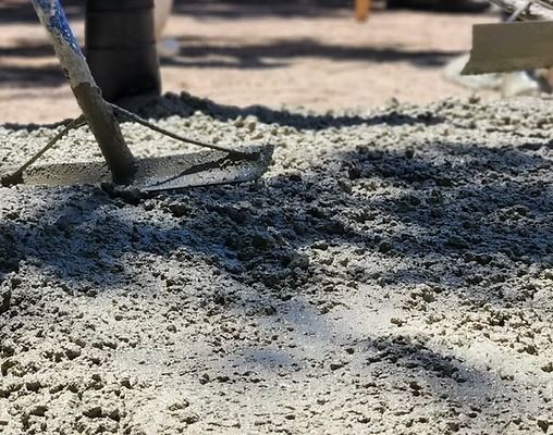 Fresh concrete being raked, creating a textured surface. Bright sunlight.