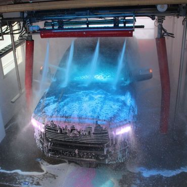 A car is being washed in a car wash with a blue light shining on it. Petit carwash 