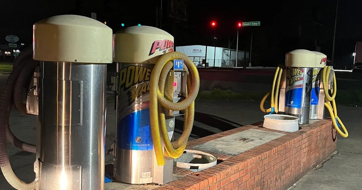 A row of car wash vacuums are lined up on a brick wall at night.