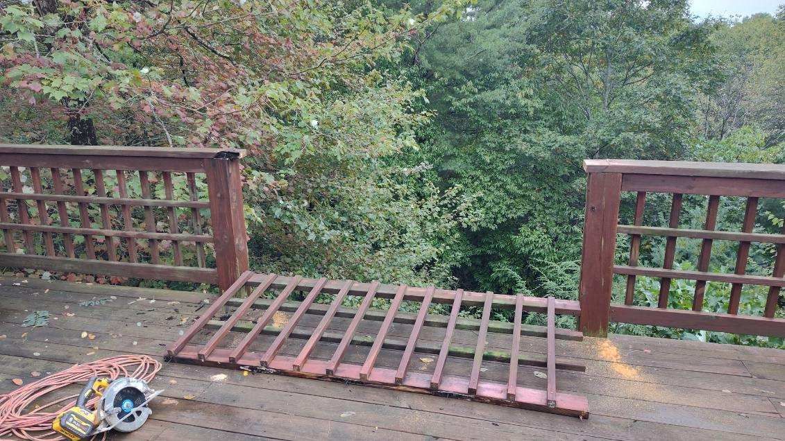 Deck with railing, a removed section lying on the deck. Power tools visible. Forest background.