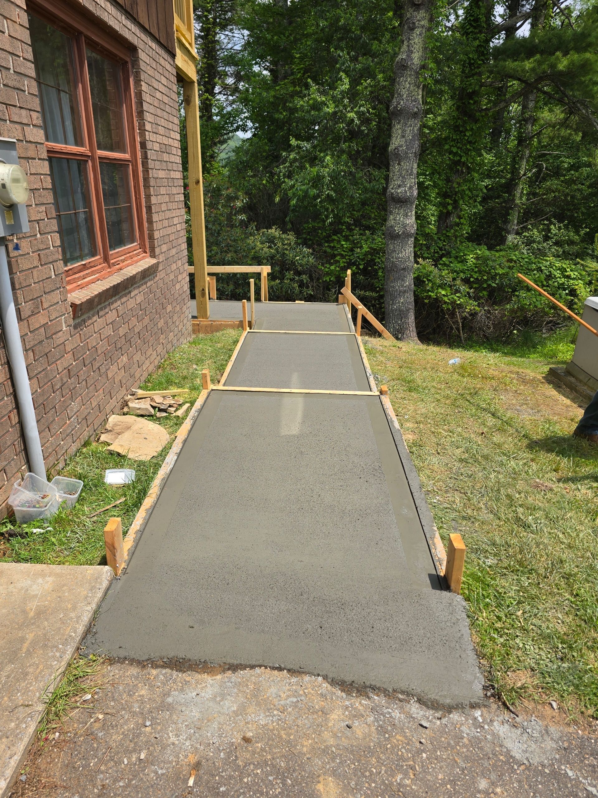Newly poured concrete ramp leading up to a wooden deck, beside a brick building.