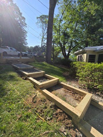 Wooden raised garden beds built into a grassy slope, with a gravel path and trees in the background.