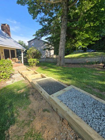 Wooden walkway with gravel sections in a backyard. House and tree in the background.