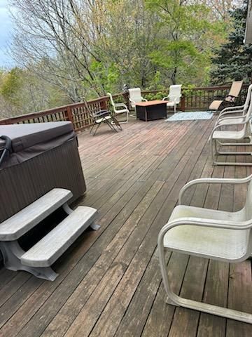 Wooden deck with hot tub, chairs, and trees in the background.