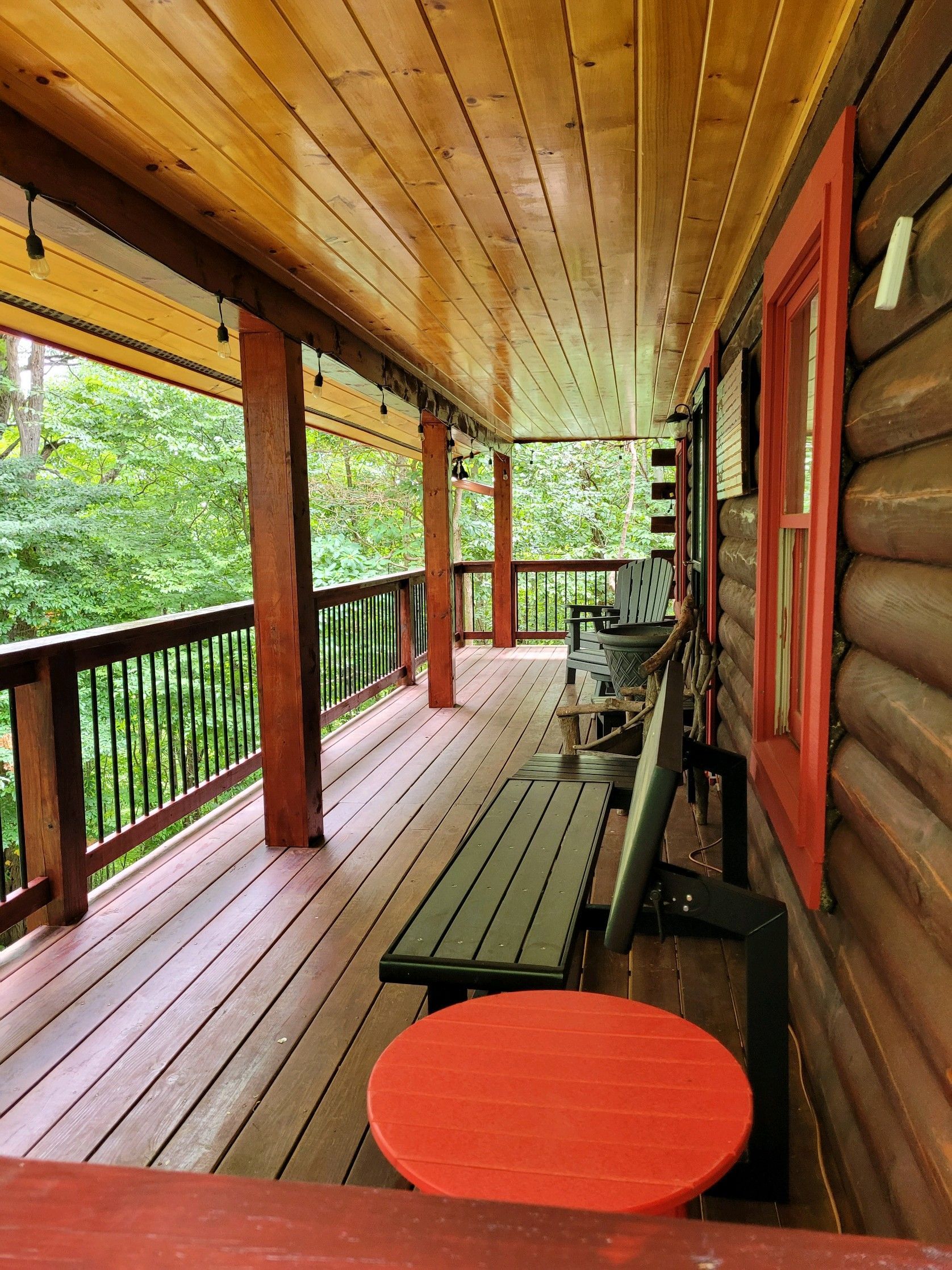 A wooden porch with a bench and a red table