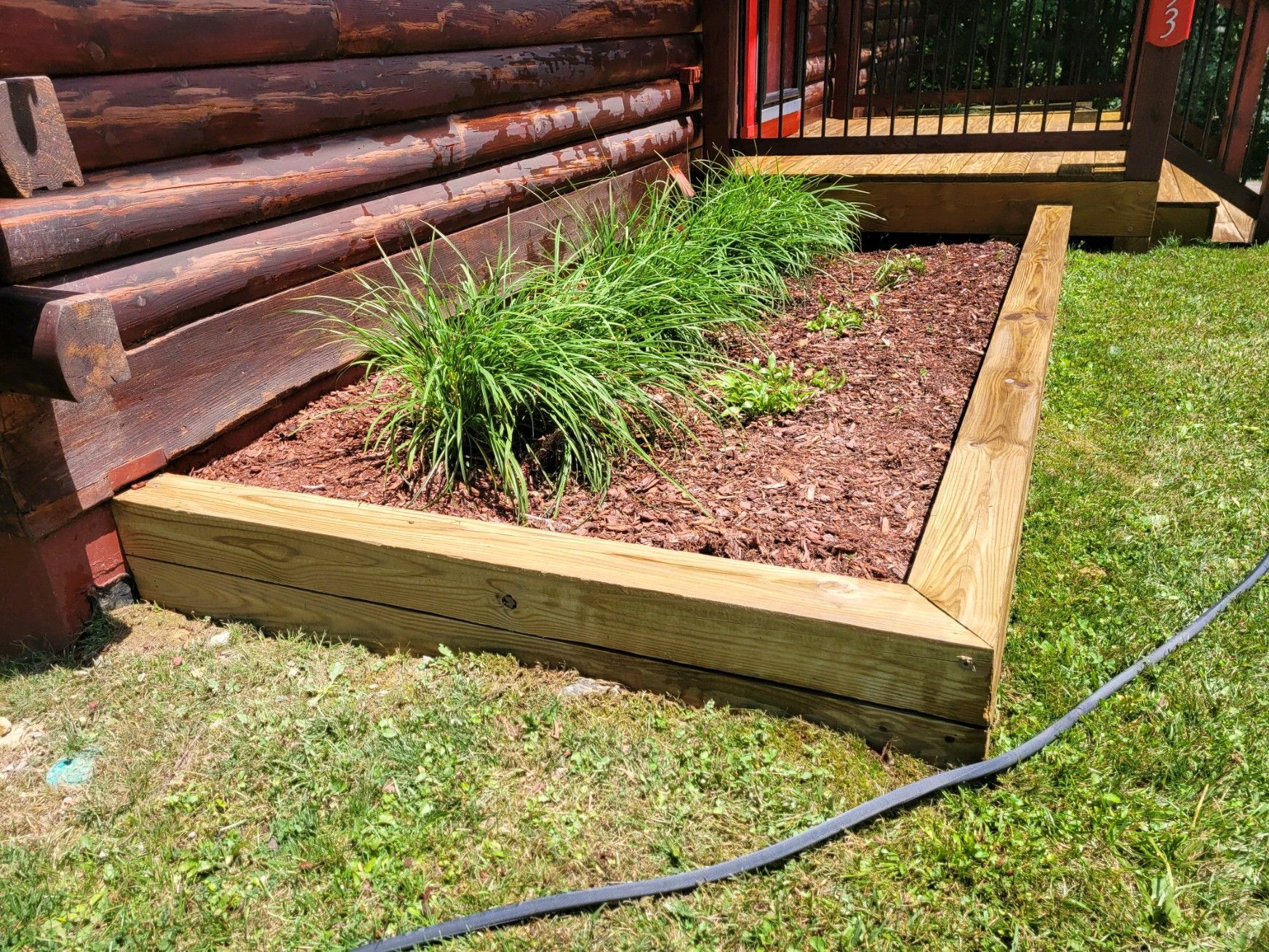 A wooden planter with plants and mulch in front of a log cabin.