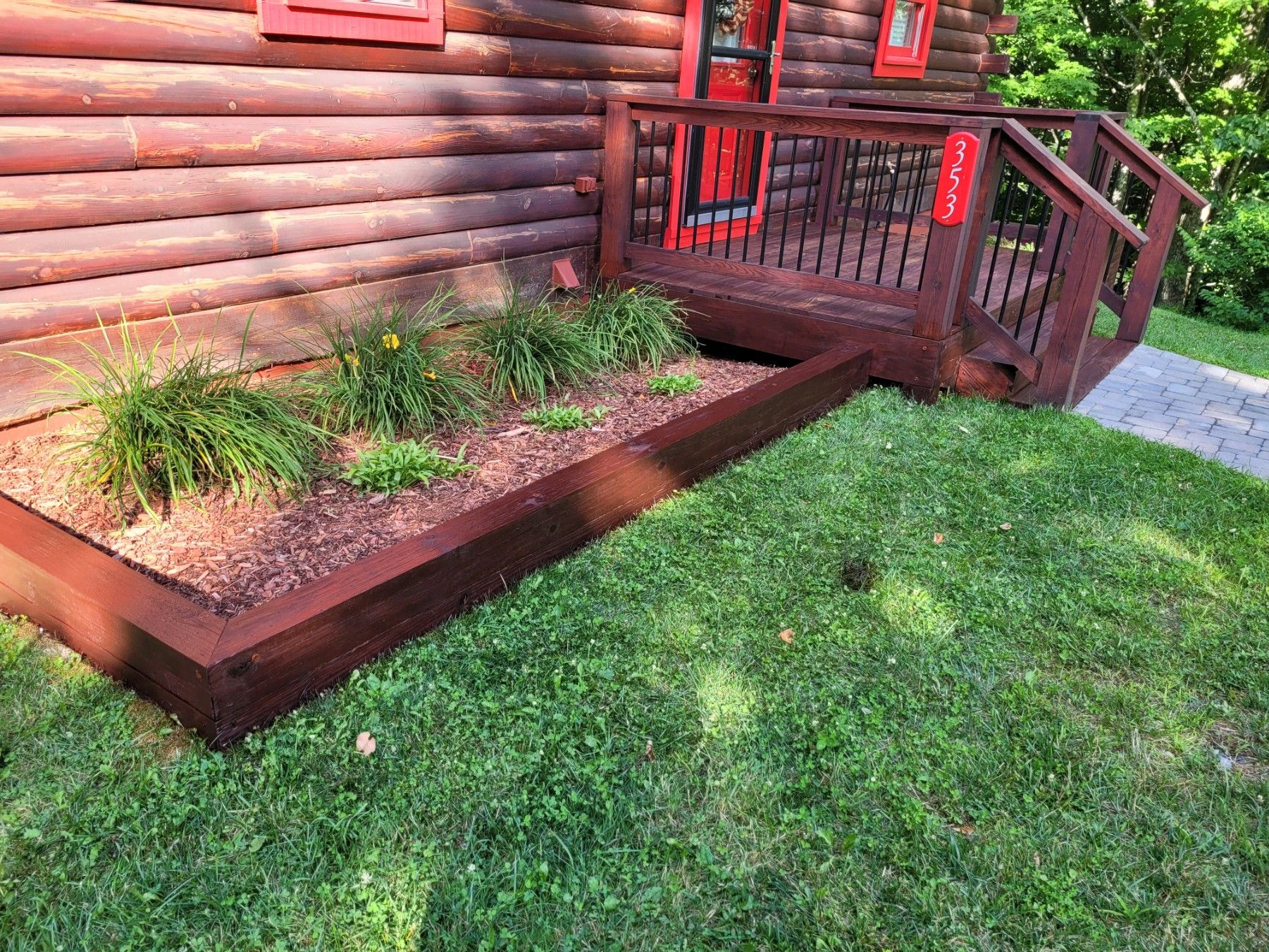 A log cabin with a wooden deck and stairs is sitting on top of a lush green lawn.