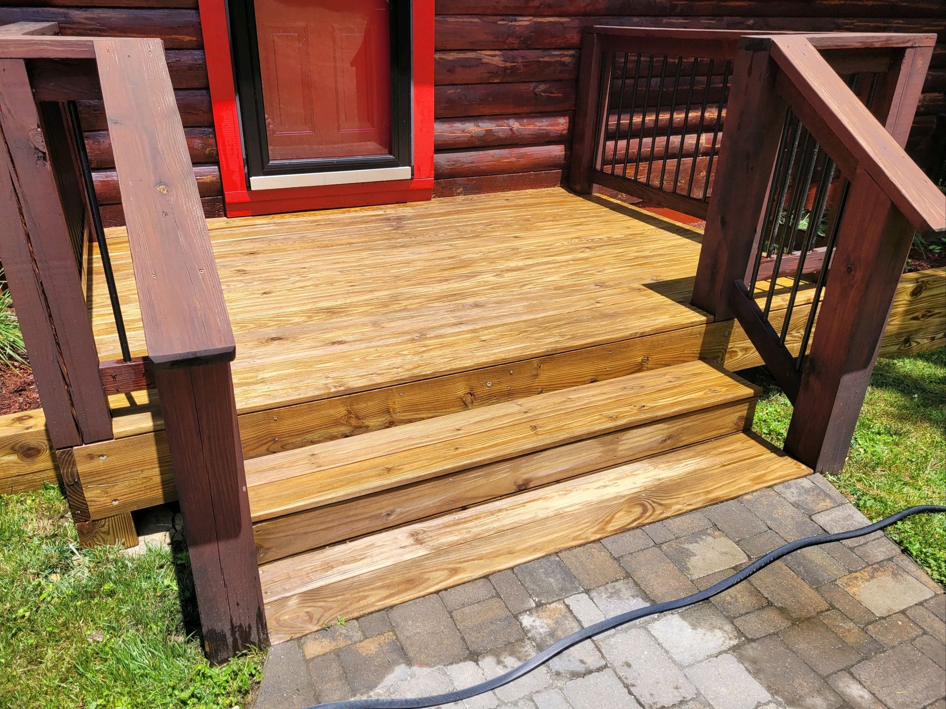 A wooden deck with stairs leading up to the front door of a log cabin.