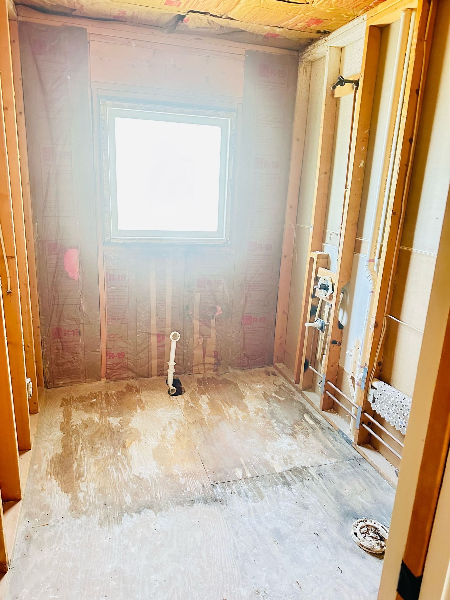 Bathroom under construction with exposed framing, window, and plumbing.