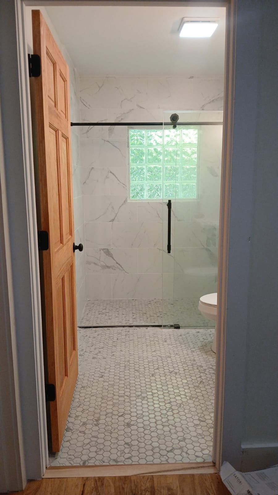 Bathroom doorway with open, paneled wooden door. White marble-look shower and mosaic tile floor are visible.