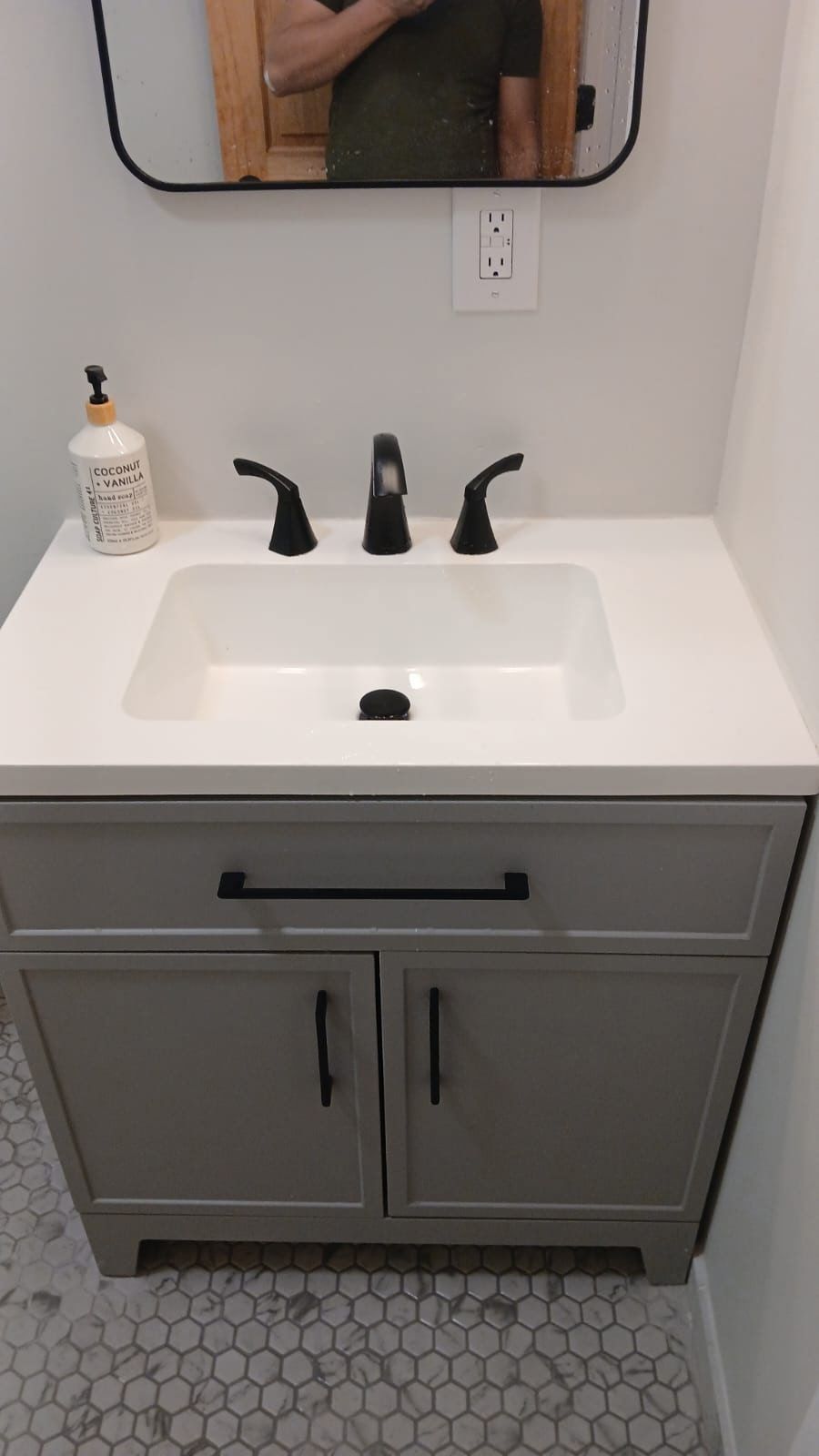 Gray bathroom vanity with black hardware, white countertop, and black faucet.