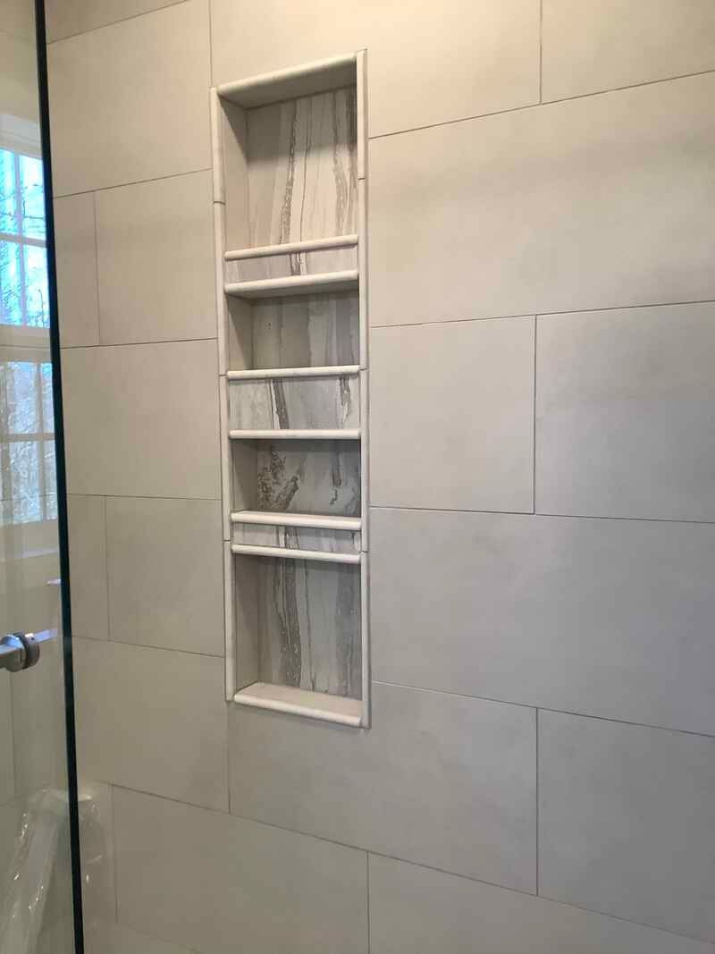 A bathroom with a shower stall and a shelf in the wall.