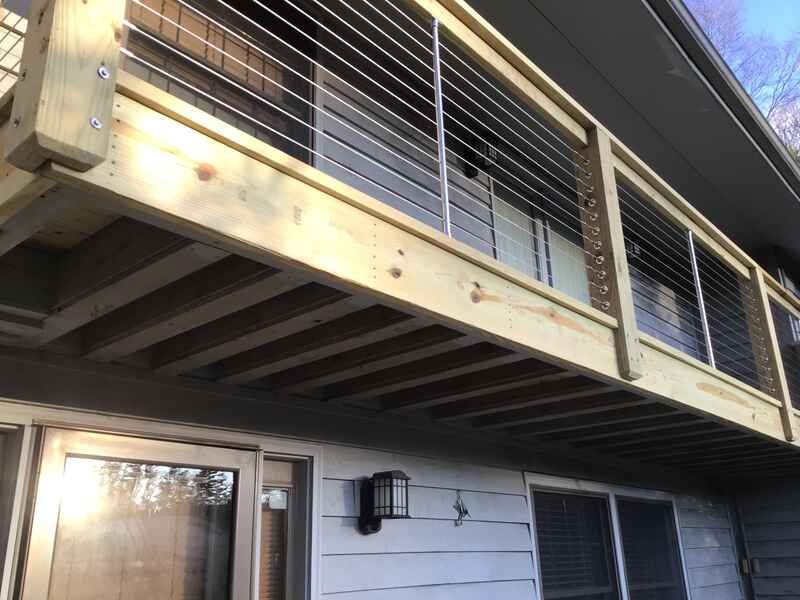 A wooden deck with a stainless steel railing is attached to the side of a house.