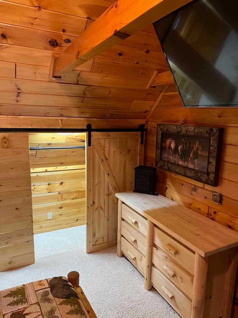 A bedroom in a log cabin with a dresser and a television.