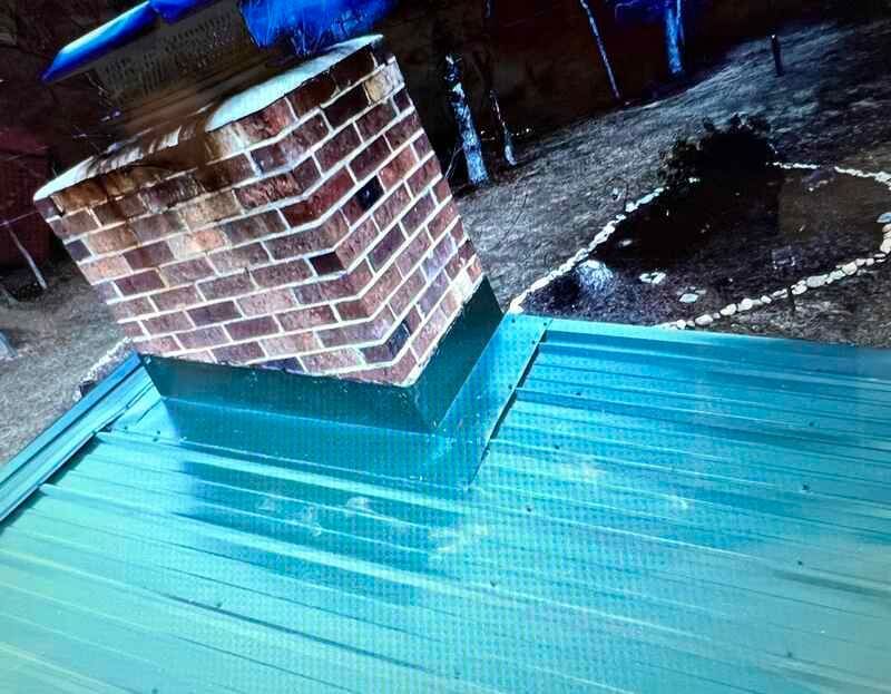A brick chimney is sitting on top of a green metal roof.
