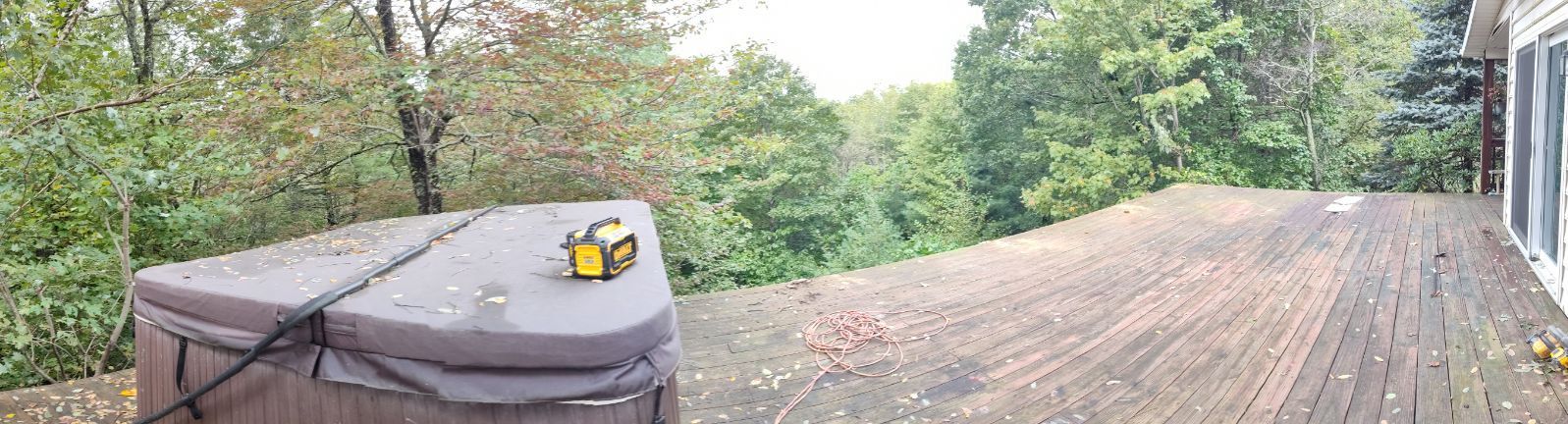Hot tub covered on a wooden deck surrounded by trees. A yellow tool sits on the cover.