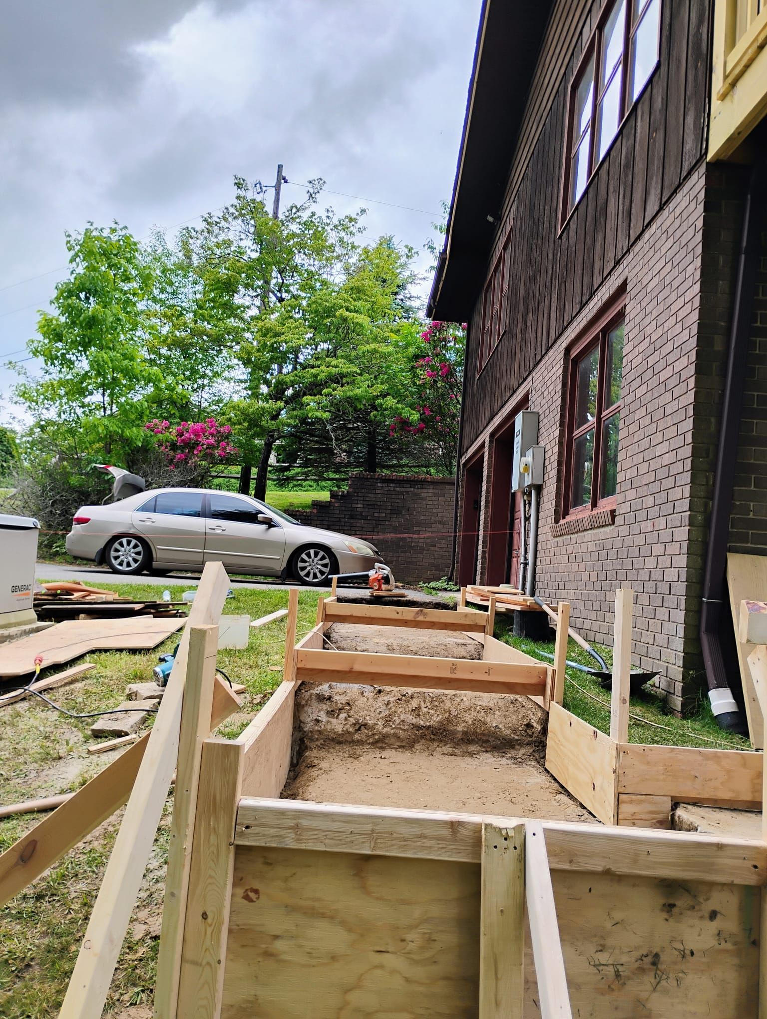 Wooden forms outline a construction site for outdoor steps next to a brick building.