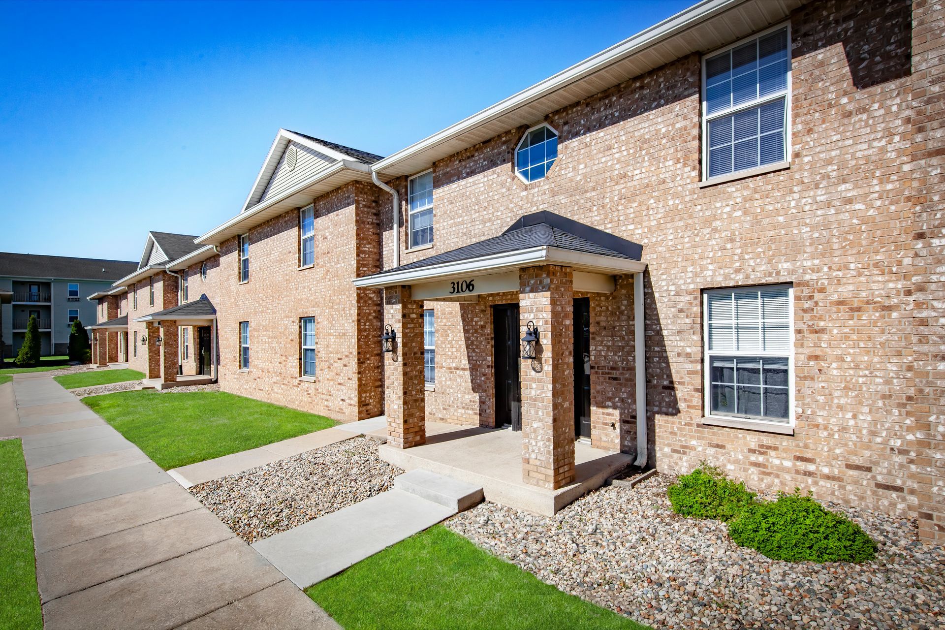 Two-story brick townhomes with dark front doors and a small tree in front.