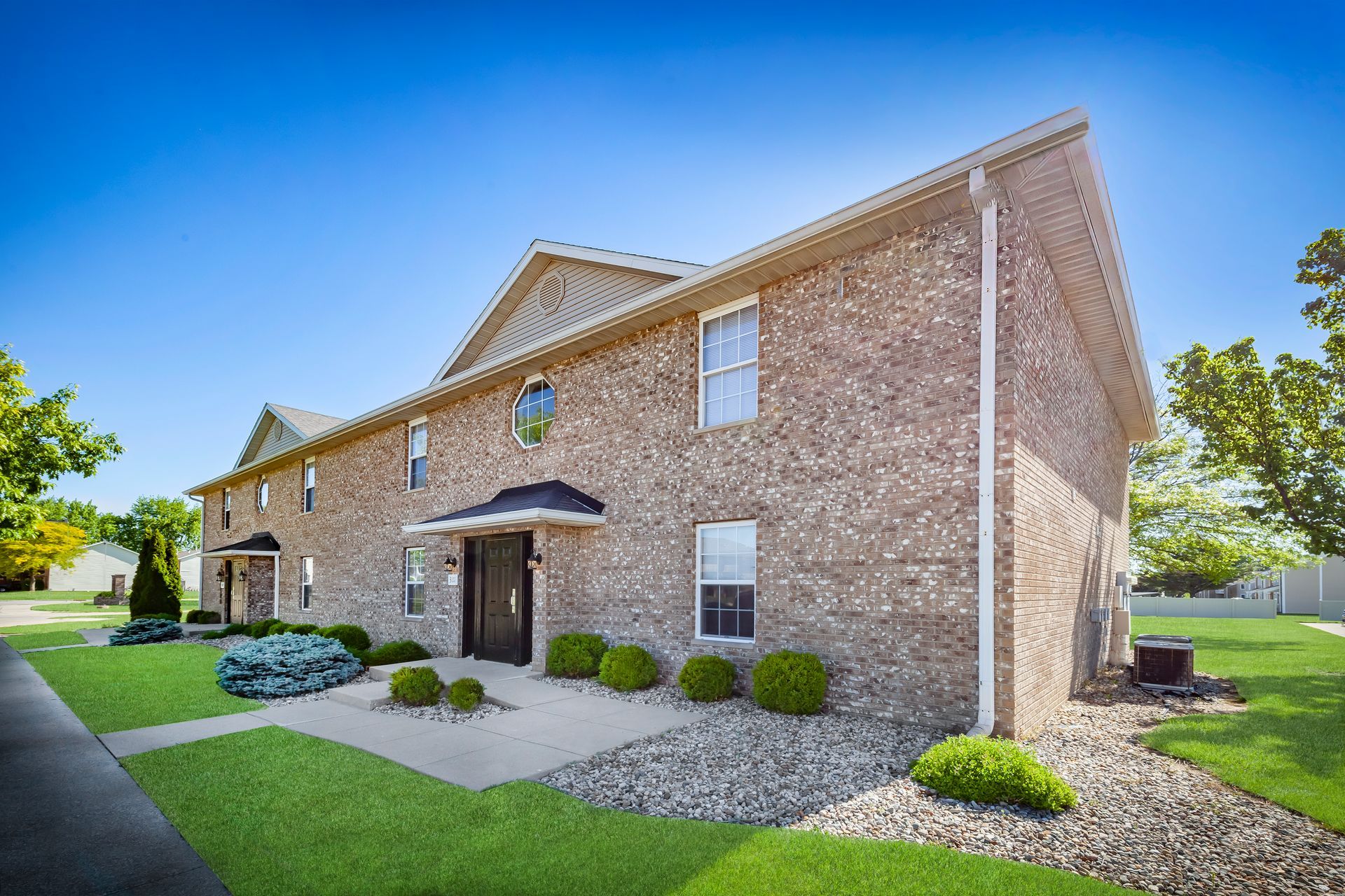 Brick apartment building with manicured lawn & shrubbery.