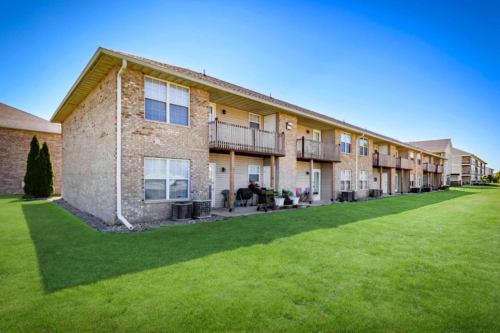 Two-story brick apartment building with balconies beside a large green lawn.