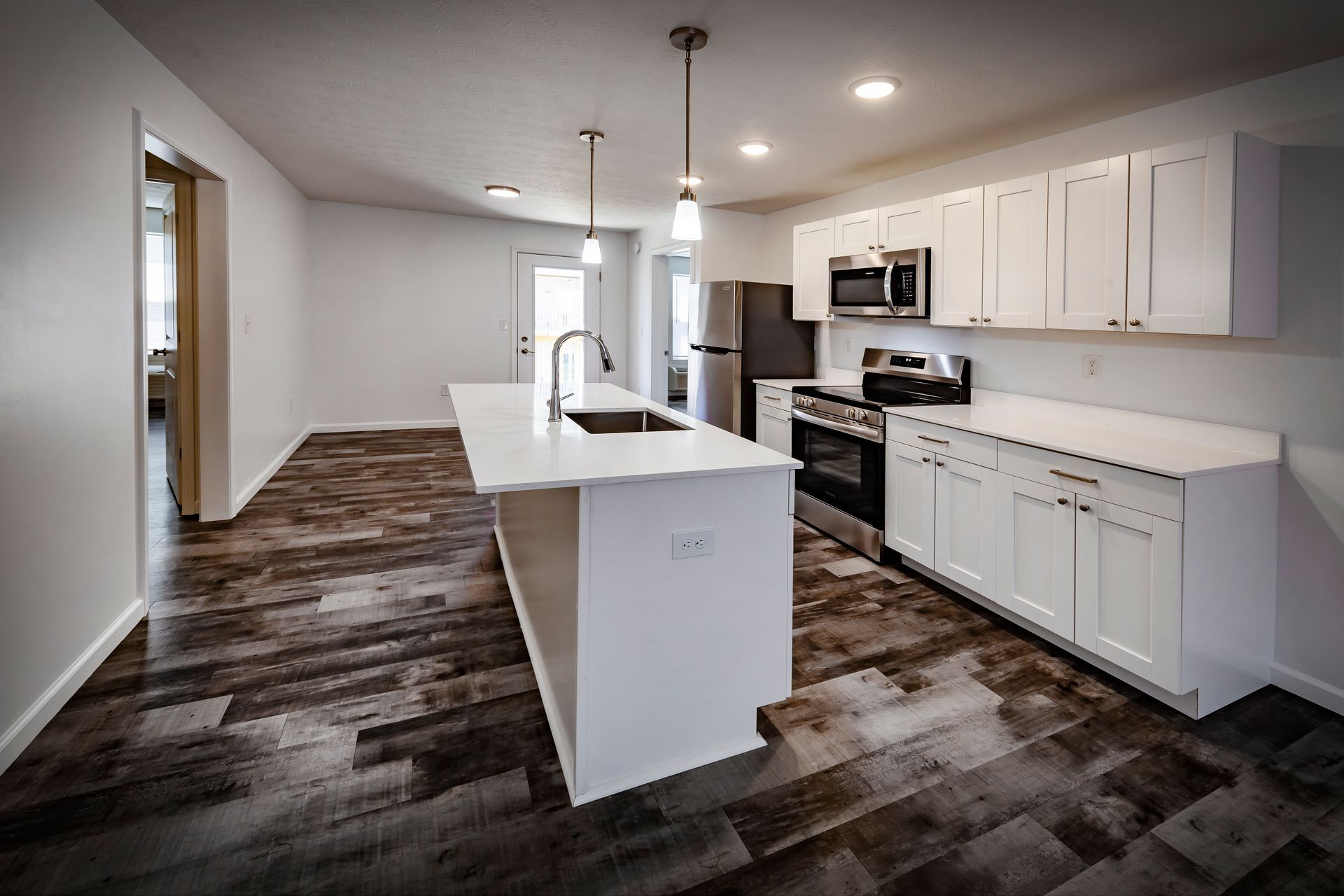 Modern kitchen and living area with white walls, cabinets, island, and dark wood-look flooring.
