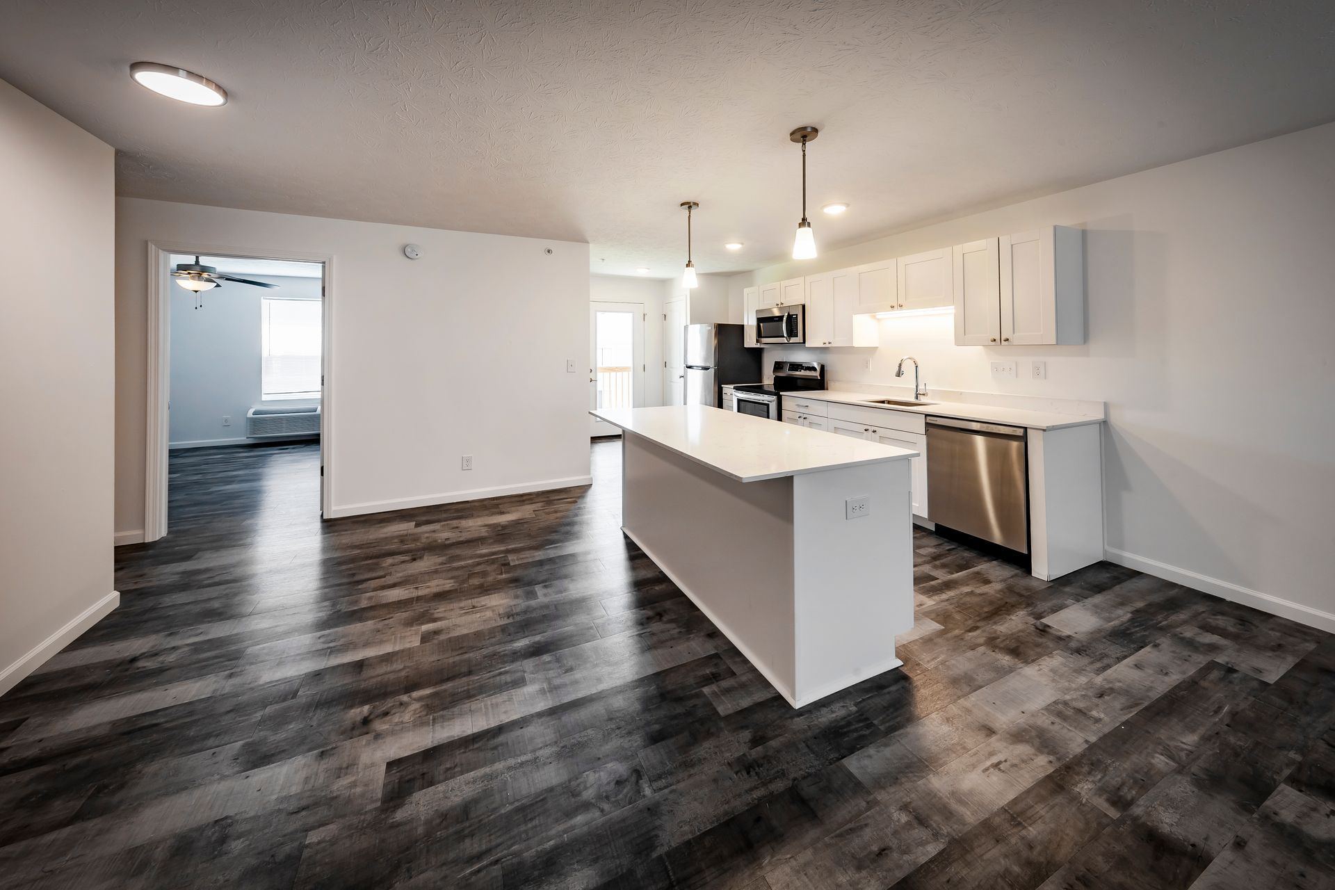 Modern kitchen with white cabinets, island, stainless steel appliances, and dark gray flooring.