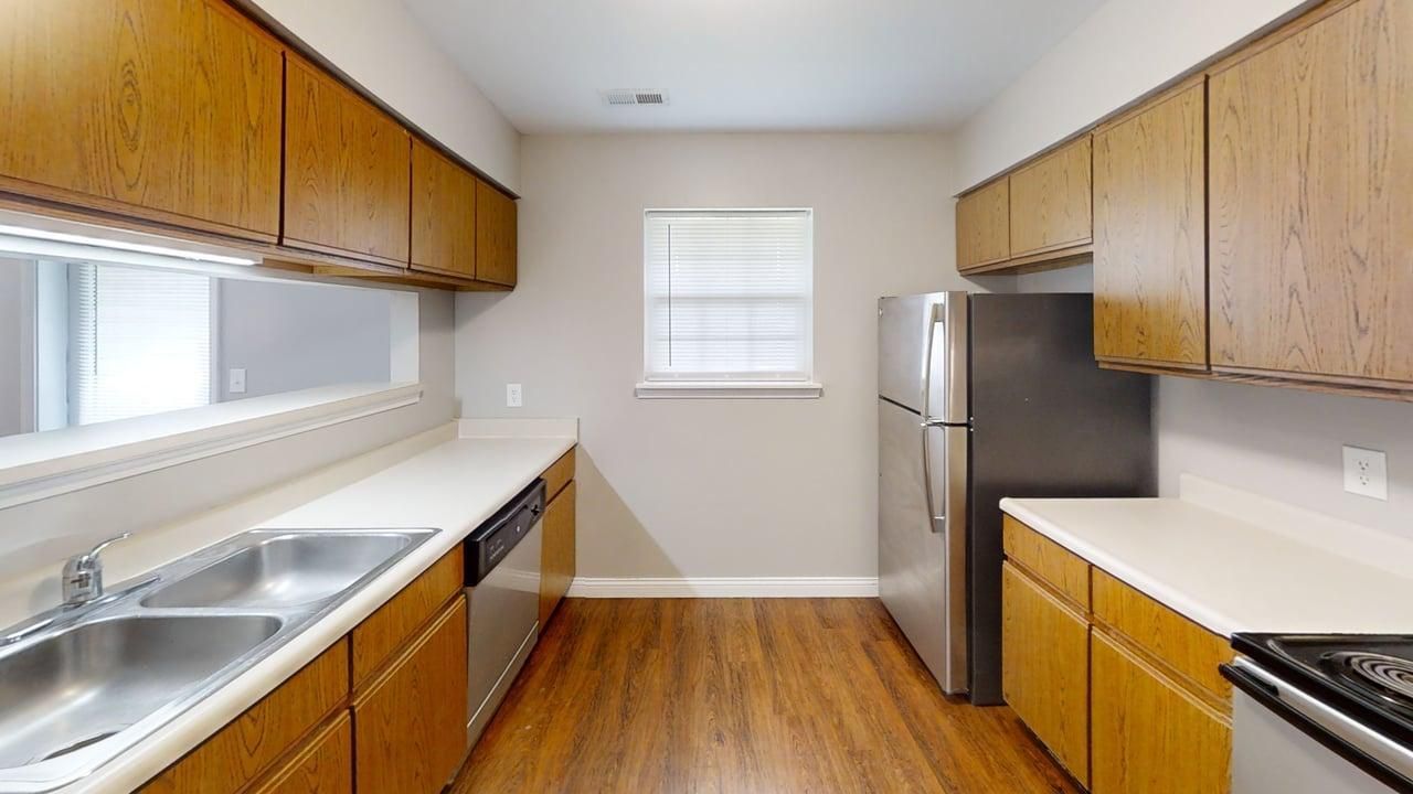 Bright galley kitchen with wood cabinets, white counters, stainless steel appliances, and hardwood floors