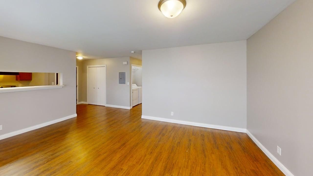 Empty living room with hardwood floors, white walls, and a ceiling light fixture