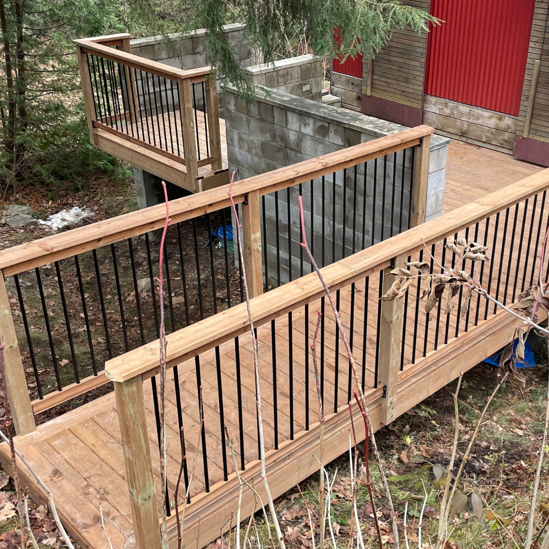 A wooden deck with a metal railing and a red building in the background.