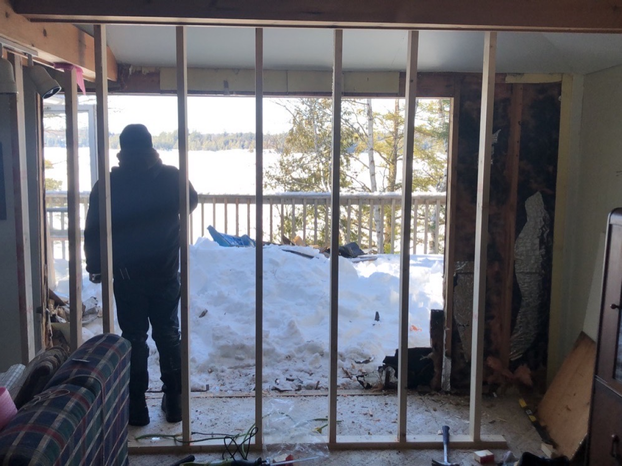 A man is standing in a living room looking out a window.