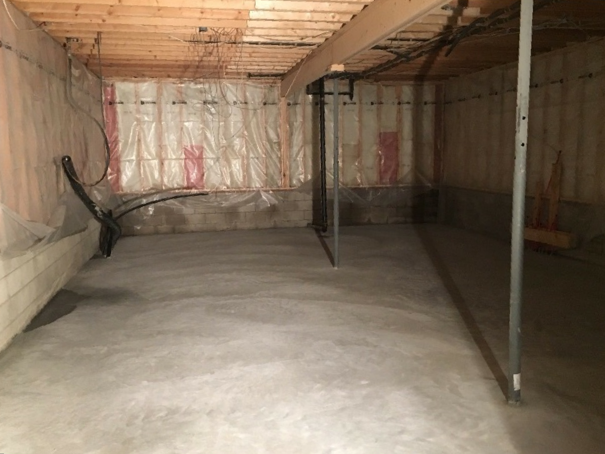 An empty basement with a concrete floor and a wooden ceiling.