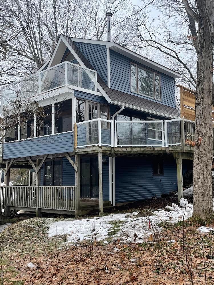 A blue house with a large deck is sitting on top of a snow covered hill.