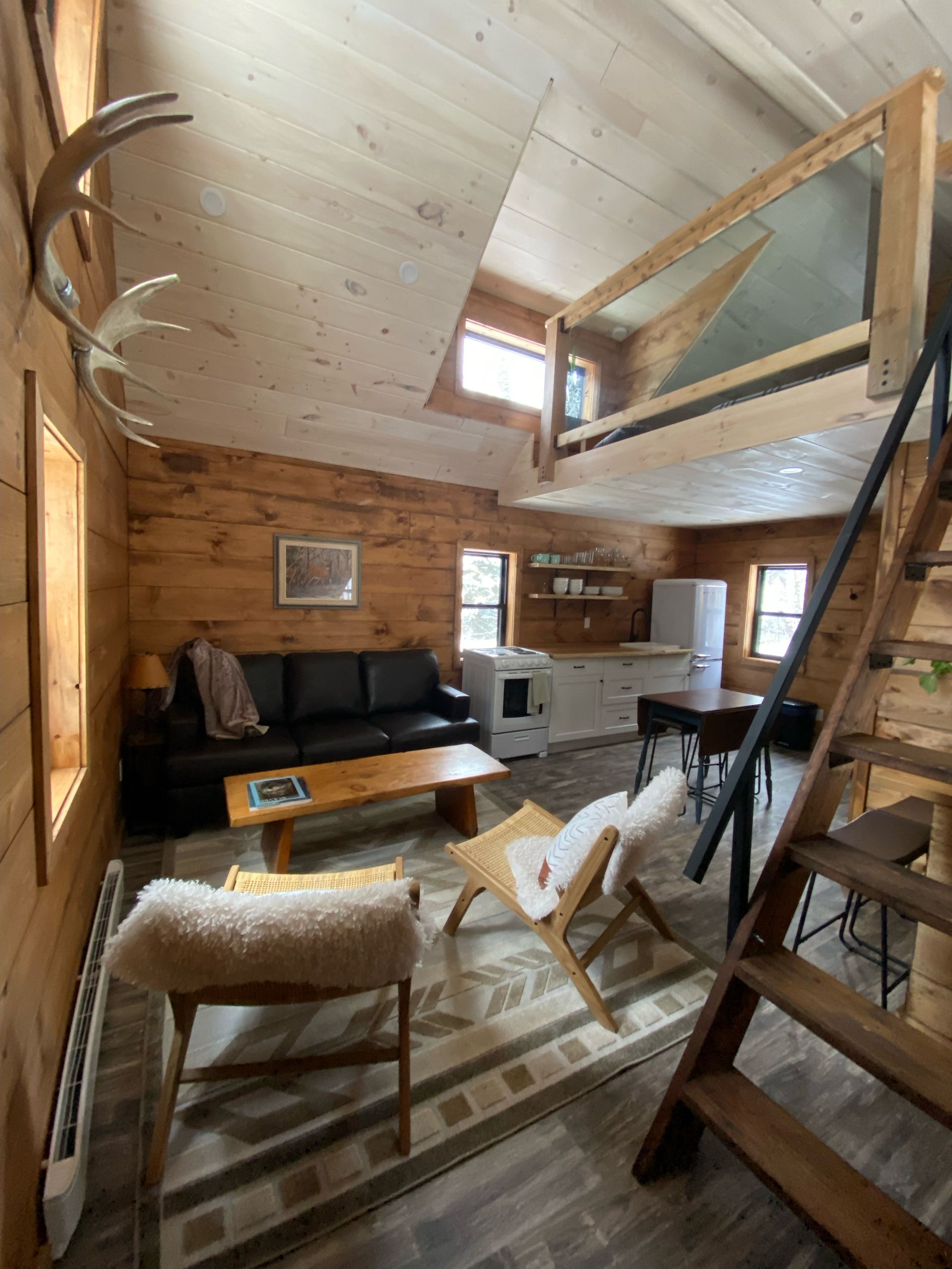 A living room with a couch , chairs , coffee table and stairs leading to a loft.